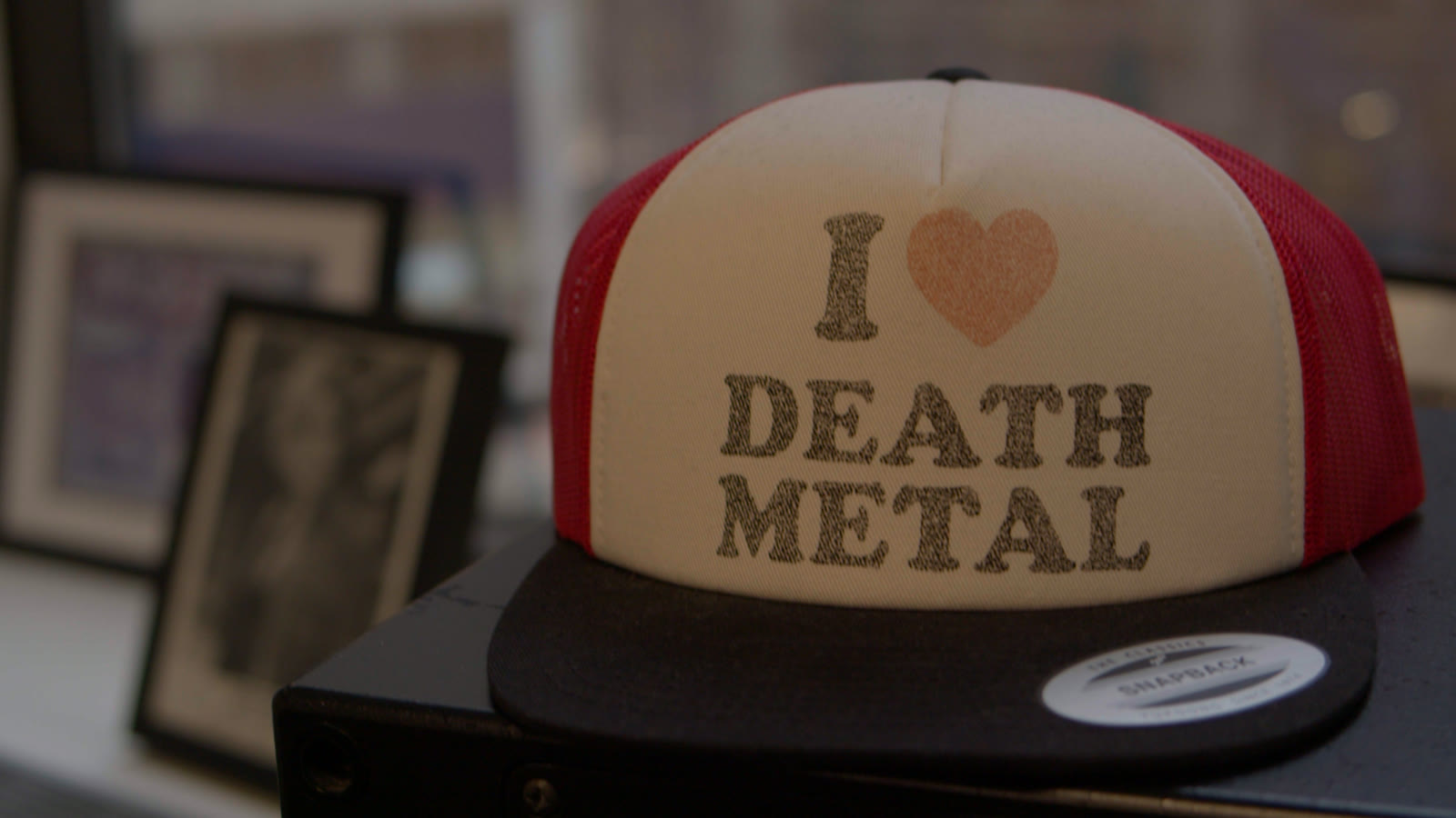 An I heart death metal cap on a plinth, framed records behind it