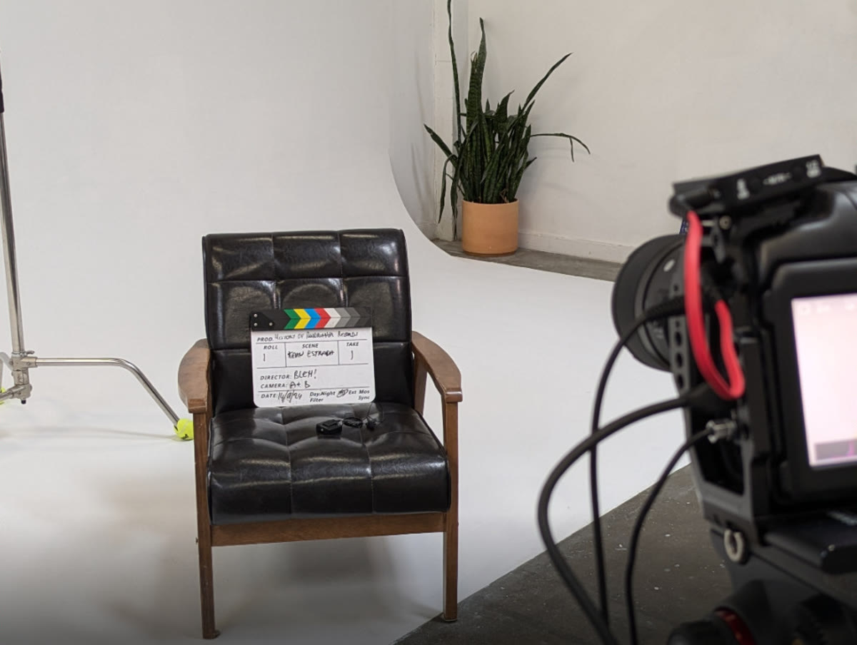 A film set: a leather chair with a clapperboard, a light stand and a cinema camera